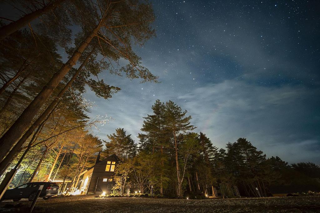 星空の下、森に囲まれたRe to Li［りとり］の建物。夜の静かな空気の中、外灯に照らされた木々と家のシルエットが浮かび上がり、上空には無数の星が輝いている。自然に囲まれたロケーションでの落ち着いた夜のひとときが感じられる。