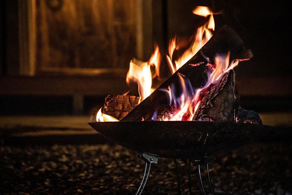 夜の屋外で焚き火台に燃え盛る薪。炎が力強く燃え上がり、暗闇の中で温かみと静けさを感じさせるシーン。