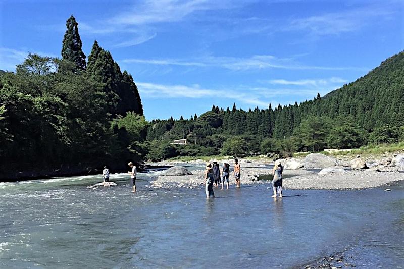 川で遊ぶ人々と緑豊かな山並み。